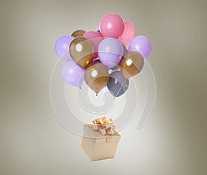 Many balloons tied to gift box on color background
