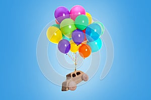 Many balloons tied to wooden toy car flying on light blue background