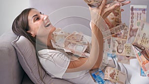 Many banknotes fly in the air overhead in slow motion. A girl lies and a lot of money falls on her. happy woman rejoices