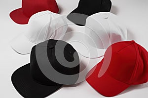 Many baseball snapback hats in different colors black, white and red laid out isolated on white surface