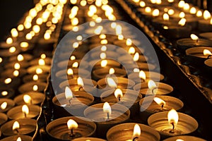 Many beautiful lit candles in a row glowing with a golden yellow light