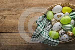 Many beautifully decorated Easter eggs in wicker basket on wooden table, top view. Space for text