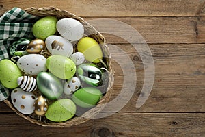 Many beautifully decorated Easter eggs in wicker basket on wooden table, top view. Space for text