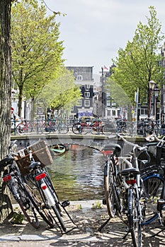 Many bikes are standing near the bridge in Amsterdam. Classic bridge over the canal in Amsterdam. The usual spring day