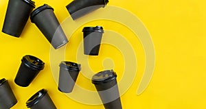 Many black take away coffee cups lay on yellow background