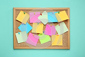 Many blank colorful notes pinned to corkboard on turquoise background, top view. Space for text