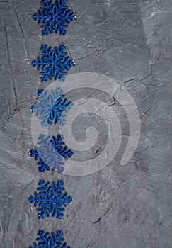 Many blue snowflakes lie in row on a gray concrete background. There is a place for a welcome text