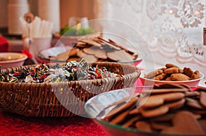 Many bowls full of heart shaped gingerbread cookies and other cookies as well as Christmas candy in a woven basket. All on a table