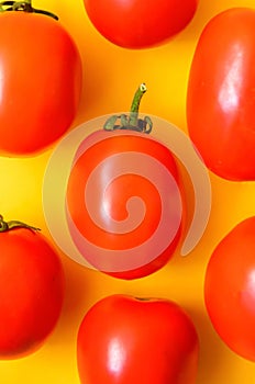 Many bright red juicy tomatoes on a yellow background.