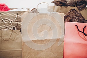 Many brown paper bags with presents on background of white wall.