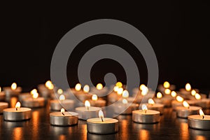 Many burning candles on table against dark background.