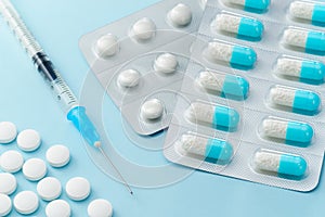 Many capsule medicines, injection syringe and pills on blue back