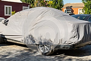 Many cars parked near suburban home driveway covered with protective tarpaulin cloth cover to protect from direct sun