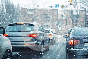 Many cars standing in row on traffic lights during snowfall in cold winter morning. Traffic jam on city street at snowstorm