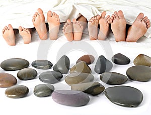 many children\'s feet peek out from under the blanket against the background of smooth stones. relaxation holiday