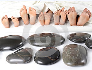 many children\'s feet peek out from under the blanket against the background of smooth stones. relaxation holiday