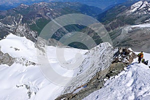 Many climbers descend a narrow and exposed snow ridge in the mountains near Zermatt