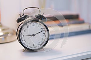 Many clock on the wall.Black alarm clock and book on white table background.