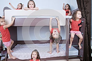 Many clone little girls on bund bed in child room in domestic life. identical child crowd. Child omnipresent and playing