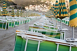 Many closed sun umbrellas and deckchairs on the sandy beach of the resort in summer