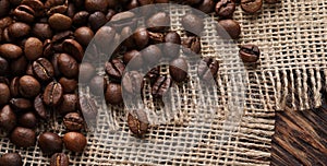 Many coffee beans and burlap fabric on wooden table, top view. Space for text