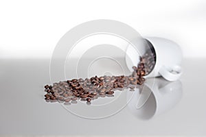 Many coffee coffee beans spilling out of a cup on a white counterspace with textspace