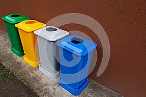 Many color recycling bins near brown wall outdoors, space for text