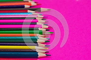 Many colored pencils lie on a pink background. Copy spase. The concept of back to school, the educational process, study at school