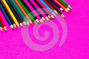 Many colored pencils lie on a pink background. Copy spase. The concept of back to school, the educational process, study at school