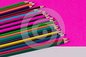 Many colored pencils lie on a white-pink background. Copy spase. The concept of back to school, the educational process, study at