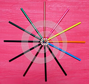 Many colored pencils on a pink background