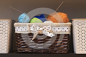 Many colored woolen threads and knitting needles lie in a wicker basket for needlework