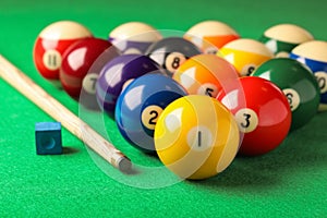 Many colorful billiard balls, cue and chalk on green table, closeup