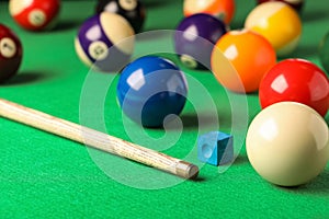 Many colorful billiard balls, cue and chalk on green table. Space for text