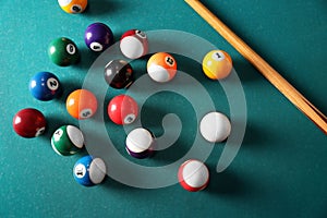 Many colorful billiard balls and cue on green table, above view