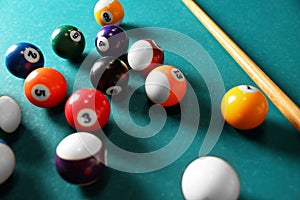 Many colorful billiard balls and cue on green table, closeup