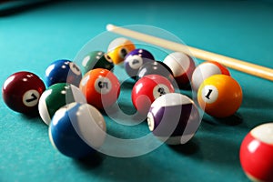 Many colorful billiard balls and cue on green table, closeup