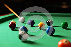 Many colorful billiard balls and cue on green table indoors