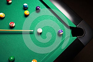 Many colorful billiard balls and cue on green table, top view