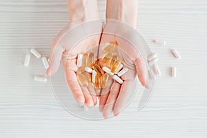 Many colorful capsules of tablets, vitamins, dietary supplements in hand on a white table close-up
