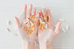 Many colorful capsules of tablets, vitamins, dietary supplements in hand on a white table close-up