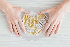 Many colorful capsules of tablets, vitamins, dietary supplements in hand on a white table close-up