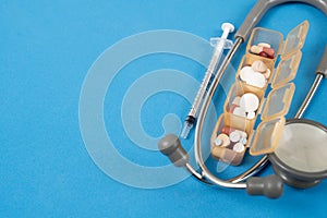 many colorful drug medicines or pill in a pillbox with and stethoscope on blue table, healthy and medicine concept