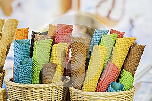 Many colorful empty wafer cones for ice cream in wicker basket, blurry background. Real scene in store