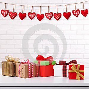 Many colorful gift boxes with ribbon bow on white table and white brick wall with vintage red heart shape garland. Valentines day