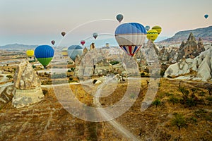 Many colorful hot air balloons flight above mountains - panorama of Cappadocia at sunrise. Wide landscape of Goreme valley