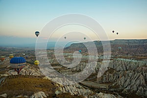 Many colorful hot air balloons flight above mountains - panorama of Cappadocia at sunrise. Wide landscape of Goreme valley