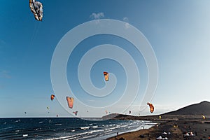 Many colorful kites on beach and kite surfers riding waves during windy day