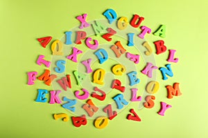 Many colorful magnetic letters on light green background, flat lay