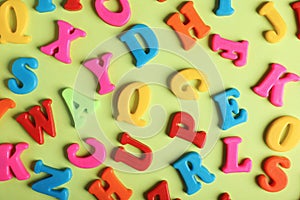 Many colorful magnetic letters on light green background, flat lay